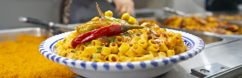 Un piatto fumante di Makrouna Fell tunisina, condito con sugo ricco di spezie, aglio e alloro, servito con carne di pollo e un tocco di autenticità mediterranea